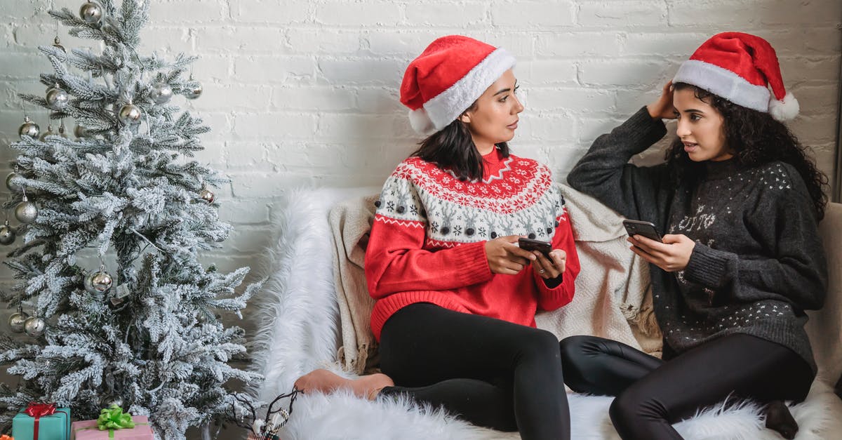 Woman in red from The 100 connection to Matrix - Multiracial young friends in warm sweaters with mobile phone chatting near Christmas tree decorated with sparkling silver baubles